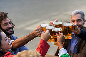 Five adults toasting with large glass mugs.