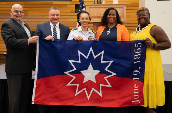 Coast Guard workforce members pose and hold up Juneteenth flag.