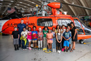 Students and Coast Guard service members standing in front of a Coast Guard helicopter