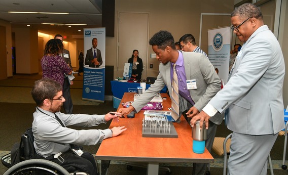 Individual in a wheelchair interacts with two people behind a registration table.