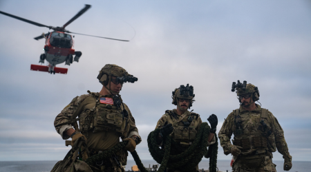 Three Coast Guard members work with a helicopter in the background