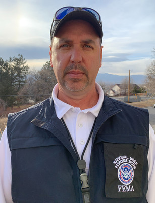 Ted Young stands outside facing the camera. He is wearing a vest over his shirt and a ballcap.