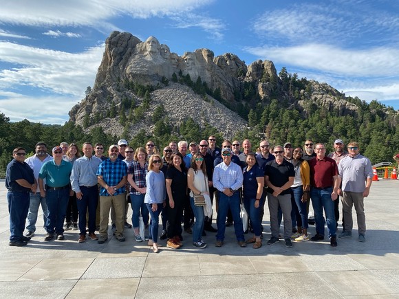 CISA employees stand in a group on a walkway with Mount Rushmore in the background