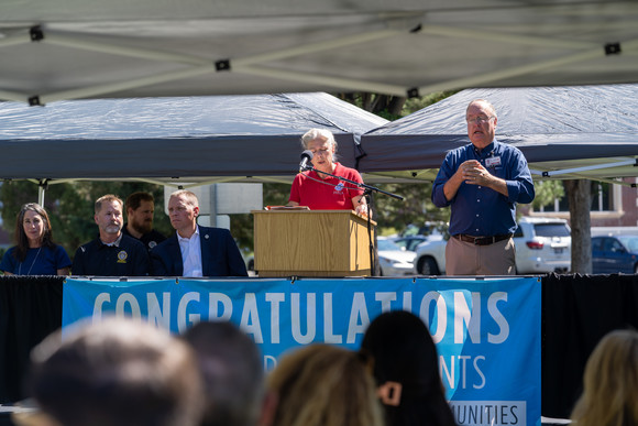 Regional Administrator Nancy Dragani speaks into a microphone at the front of an outdoor audience.