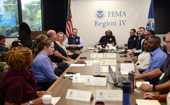 A group of people sit around a conference table. Nametags are atop the table. On the wall behind the table reads "FEMA Region IV" with the FEMA logo