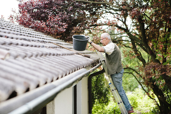 A man on a ladder cleaning off the roof of a house