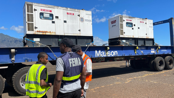 Two people in front of a truck with generators. 