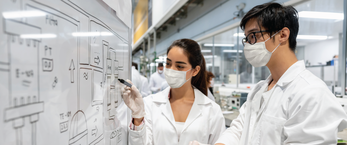 Students in masks and lab coats stand at a white board