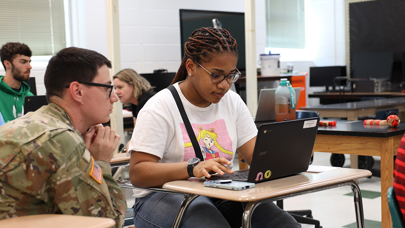 Service member sitting near student at desk