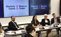 Assistant Secretary Jereza in boardroom setting with several presenters in front of backdrop with text "Electricity Canada | Electricite Canada"