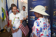 Assistant Secretary Katie Jereza holds a U.S. flag and speaks with a participant at the Great American State Fair, DOE history poster visible.