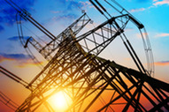 Low-angle view of a transmission tower silhouetted against a vibrant sunset sky transitioning from deep orange to blue.