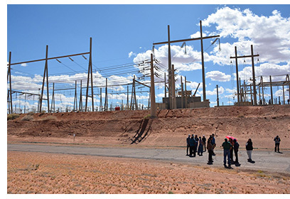 A group of people stand near a large outdoor electrical substation