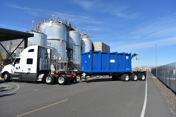 A large truck transporting a trailer with a large blue container on the trailer.