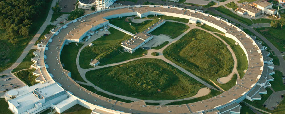 Aerial photo of the Advanced Photon Source (a large ring-shaped building with a parking lot and other white buildings around it)
