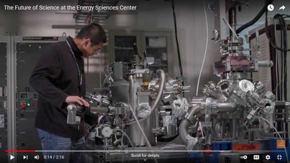 Screenshot of a video with an Asian man working with a very complex piece of metal scientific equipment