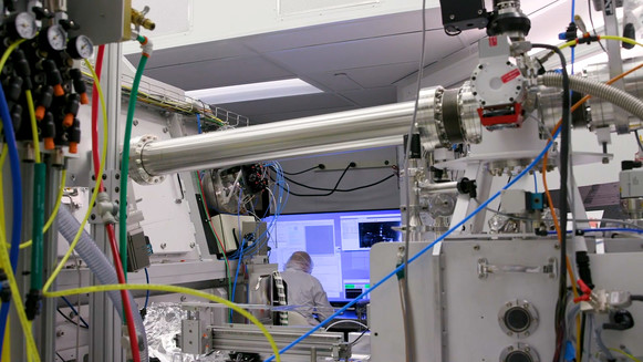 Photo of the inside of a lab with a person in a clean suit at a computer and complex scientific equipment around them