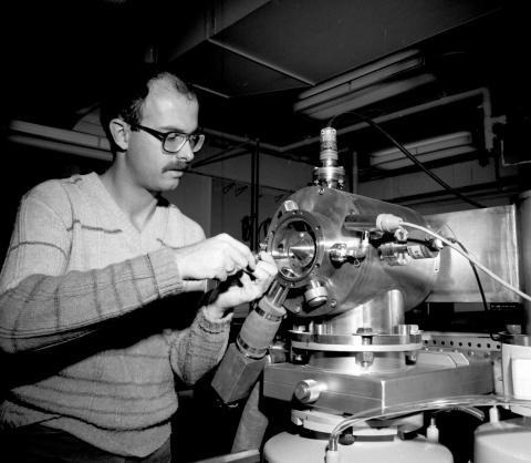 Black and white photo of Sam Houk (white man in a sweater) working with a mass spectrometer