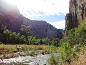 Photo of a river flowing through a valley with grasses around it and two large cliff walls on both sides