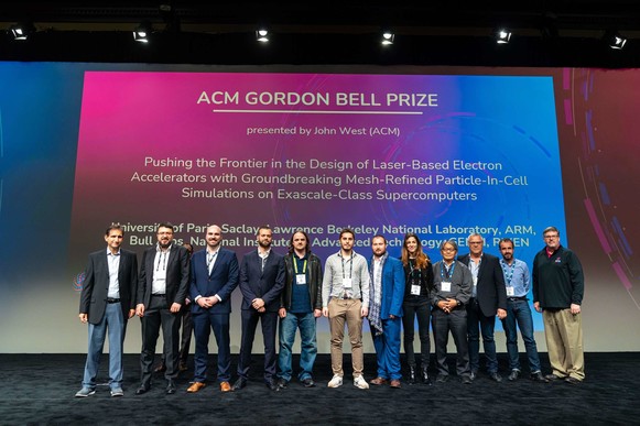 Photo of a group of 12 people (mostly men) standing in front of a screen that says "ACM Gordon Bell Prize - Pushing the Frontier in..."