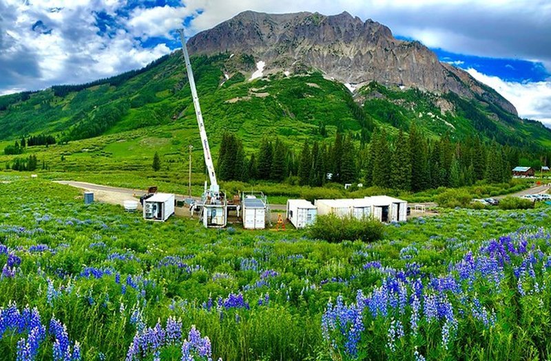 Photo of a valley in the Colorado River basin, with flowers and grass in the foreground, white equipment boxes, and a mountain