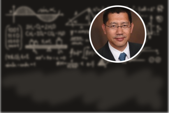 Photo of Ming Ye (an Asian man in a suit) against a background that is a blackboard with blurred equations