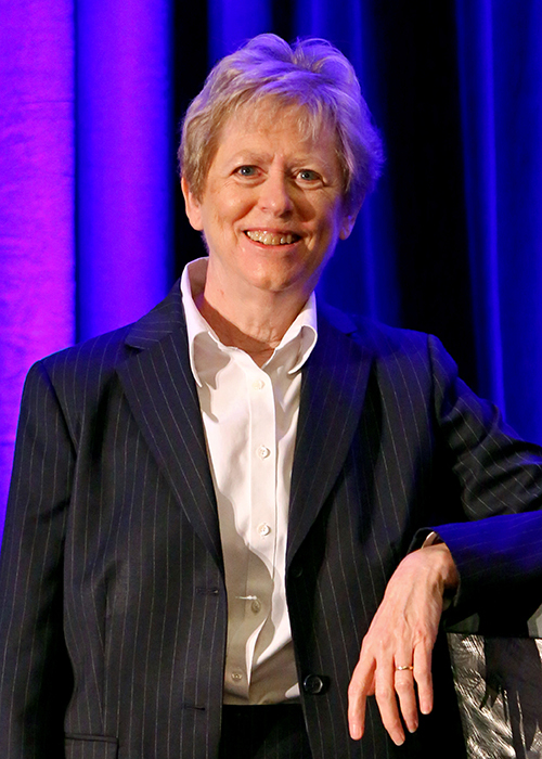 Photo of Barbara Helland (a white woman in a suit) standing in front of curtains