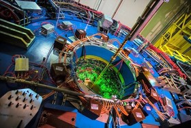 Photo of the Relativistic Heavy Ion Collider, a large metal ring with wires all around it and glowing green from the inside