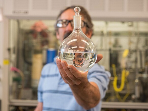 Photo of Rich Hallen holding flask with a sample of jet fuel upgraded from ethanol made from industrial waste gases.