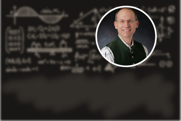 Photo of Paul Romatschke (a white man in a green vest) against a background of a blackboard with blurred equations
