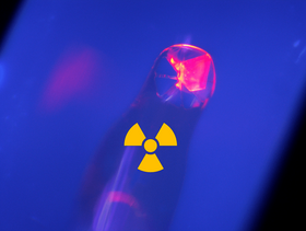 Photo of a curium compound, which glows pink against a bluish background with a radioactive symbol over it 