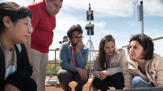 Six people in casual clothing of different races looking at atmospheric measurement equipment