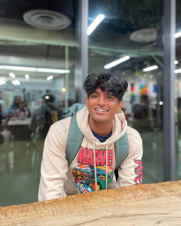 Avi Vadali (a young South Asian man in a sweatshirt with Marvel heroes on it) sitting at a table in a lab
