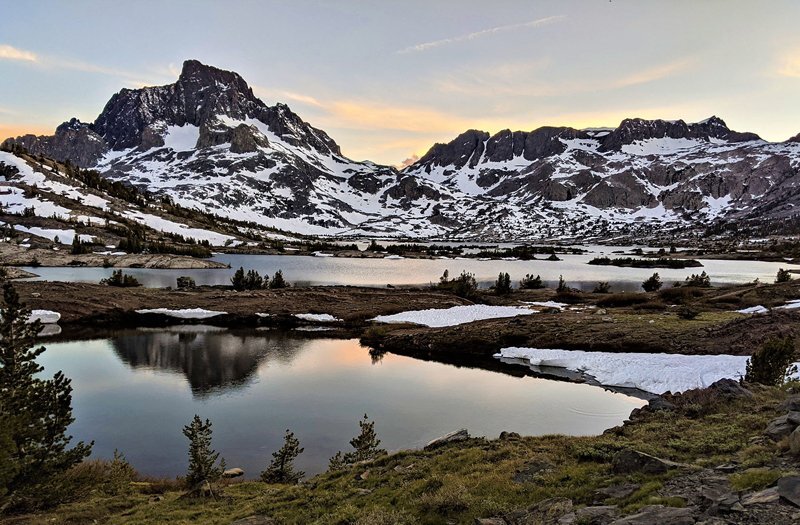 Snowy mountains rising up behind lakes with pine trees around them