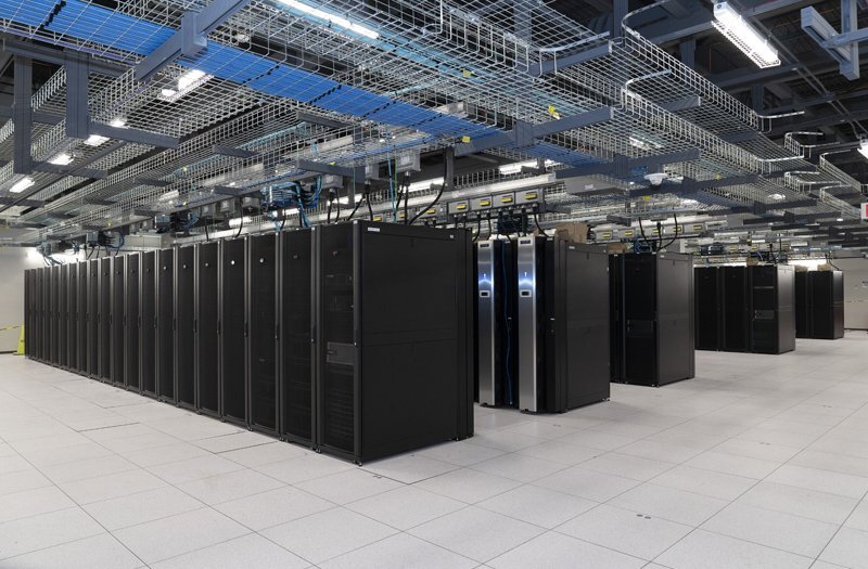 A data storage facility with rows of supercomputer cabinets and a metal grid overhead on the ceiling