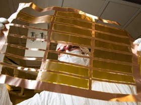 Isaac Arnquist (a person in a clean room suit) looking at a copper and gold-colored sheet with gaps in it