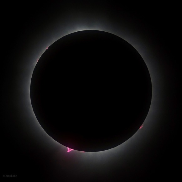 Total solar eclipse with the moon in front of the sun and small areas of pink around it