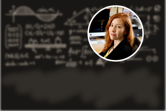 Sigrid Elschot (a white woman in a black jacket and yellow shirt) with a background of a blackboard with blurred equations