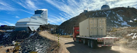 A truck driving up a dirt road in the mountains to a large white, blocky building