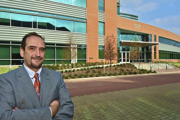 Daniel Vrinceanu (a white man in a striped suit) standing outside of a brick building with large glass windows
