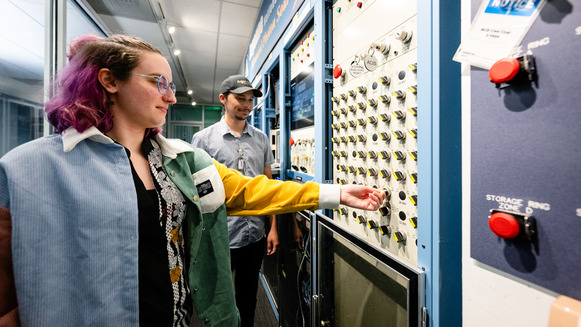 Rebecca Weber turns a key on a wall of switches  that enables the shutter at the 27-ID beamline while Matt Spilker looks on