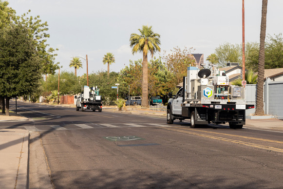 Two pickup trucks with the Brookhaven Lab logo and instruments in the back driving down a road with palm trees on the sides