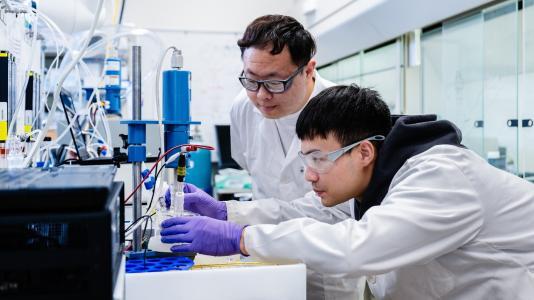 Researchers Haozhe Zhang and Jianxin Wang working with chemistry equipment to experiment with catalysts.