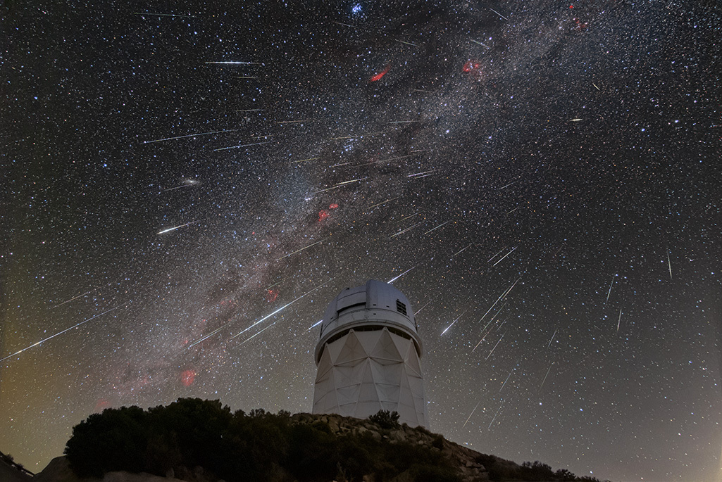 An astronomical observatory (a cylinder-shaped building with a dome on top) with the Milky Way and comets in the sky behind it