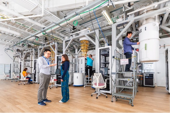 Five people in a laboratory with a wooden floor and metal beams supporting various quantum computing equipment
