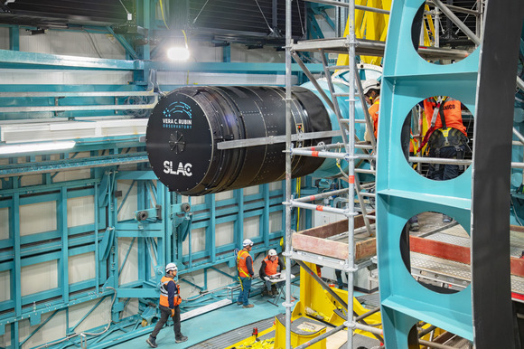 A camera the size of a car being positioned in place with scaffolding and workers in safety gear around it