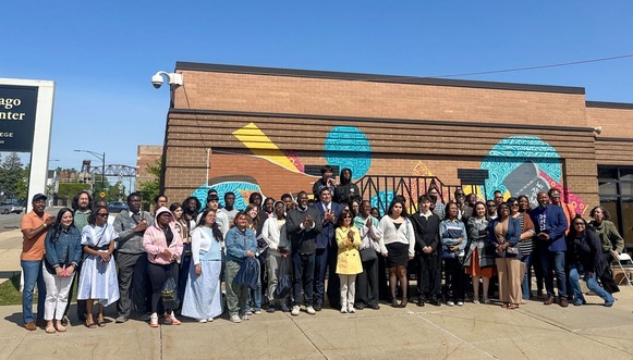 Group of high school students standing in front of a brick building with a colorful, abstract mural on it
