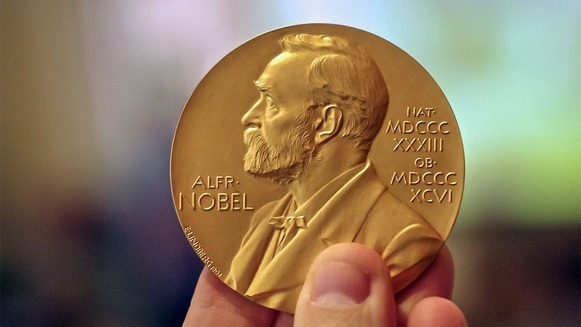 Image of a hand holding the Nobel Prize medal, which is gold with a picture of Nobel on it