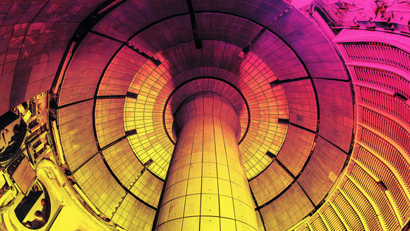 The inside of a fusion tokamak (a donut shaped machine with a column in the center) lit in pink and yellow light