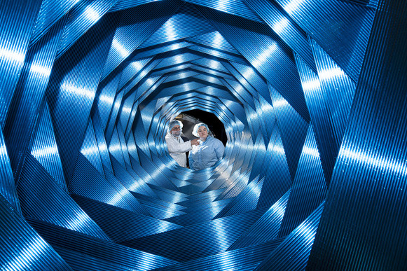 Layers of blue, ridged panels in a flower pedal-like configuration. There is a hole in the center through which we can see two scientists.